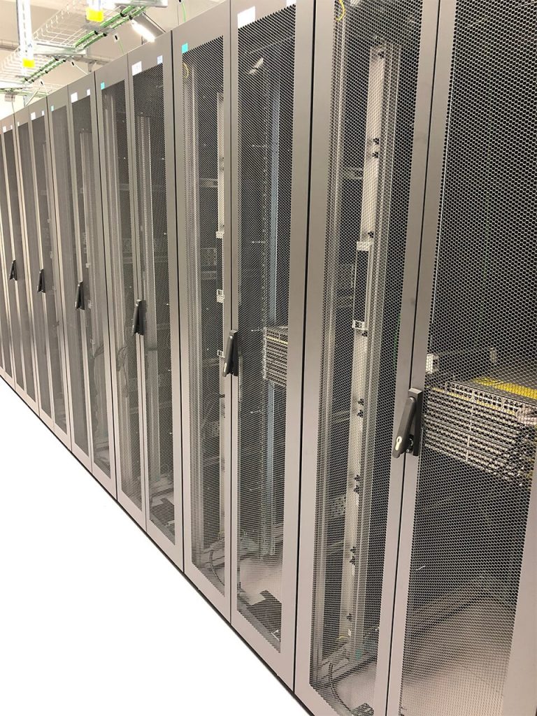 Row of server racks in a data center with mesh doors, visible cabling, and equipment inside each cabinet.